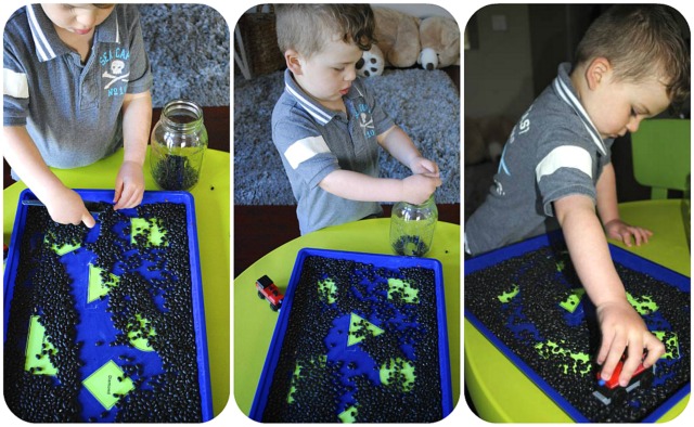child playing with trains and filling and pouring with bean sensory tray
